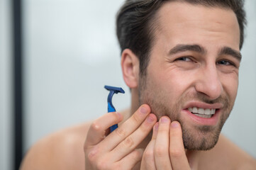 Young man shaving and looking disturbed