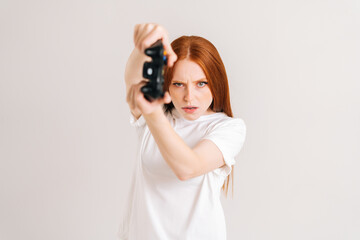 Studio portrait of focused young woman playing video game with controller looking at camera on white isolated background. Happy lady using joystick on console enjoying online game.