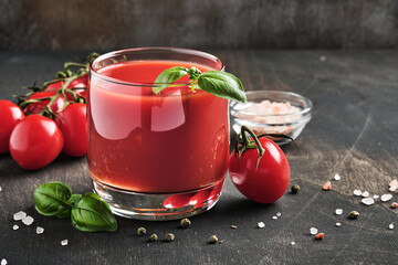 Glass of fresh tomato juice, salt, basil and tomatoes on  wooden stand  on old wooden background. With copy space.