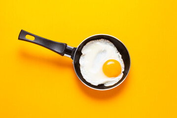 Scrambled, frying  eggs from one egg in a small pan on yellow background