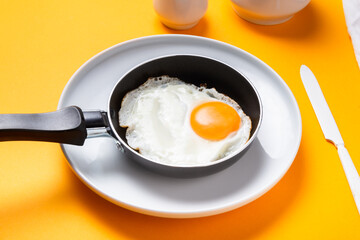 Scrambled, frying  eggs from one egg in a small pan on yellow background