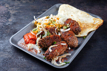 Traditionelle kroatische Cevapi als würzige Fleischbällchen mit scharfem Ajvar, Pita Brot und Kraut Karotten Salat serviert als close-up in einem Metall Tablett