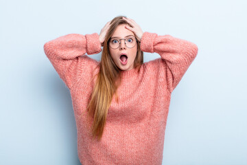 caucasian red hair woman feeling horrified and shocked, raising hands to head and panicking at a...