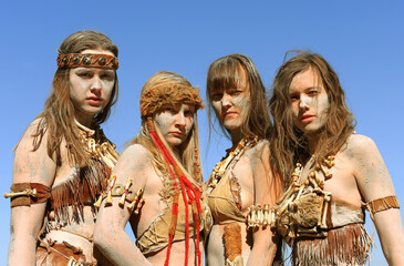 A Group of women are dressed as Neanderthal warriors. 
Their bodies and faces are covered with mud,...