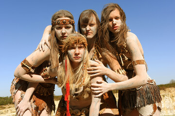 A Group of women are dressed as Neanderthal warriors. 
Their bodies and faces are covered with mud,...