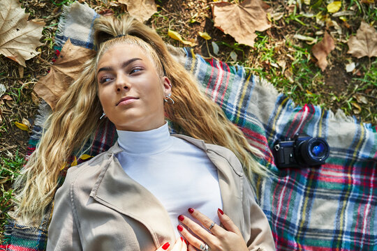 Pensive female lying on plaid with dry leaf in park