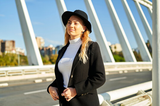 Young positive woman in black jacket and hat on bridge