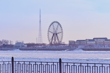 View of the Chinese Amusement Park with a Ferris wheel from the city of Blagoveshchensk, Russia through the embankment fence. Winter morning. The Amur River is ice-bound.