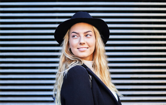 Stylish smiling young woman in black jacket and hat