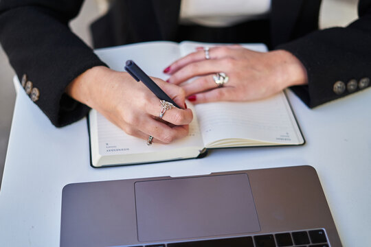 Anonymous freelancer woman writing notes while working with laptop in cafe