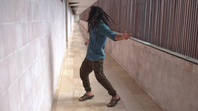 Cheerful and Happy Smiling Young Indian Man with Beard and Hair Braided in Dreadlocks Casual Clothes Actively Dancing in a City Building