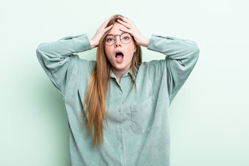 caucasian red hair woman feeling horrified and shocked, raising hands to head and panicking at a...