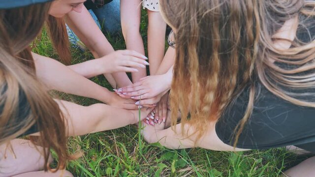 Girls friends join hands on the grass in the park.