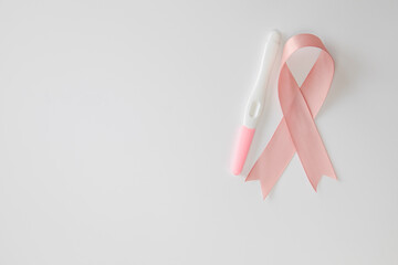 Pink satin breast cancer awareness ribbon with blank pregnancy test isolated on white background top view