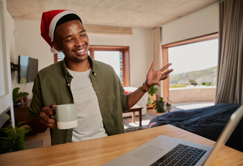 Young adult black male casually talking on online call, wearing Christmas hat. Sitting at kitchen counter using laptop.