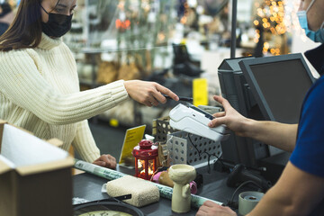 Young woman checks out using the phone through the terminal in the store. Social distancing and coronavirus covid prevention. Maintain a safe distance from others at the store