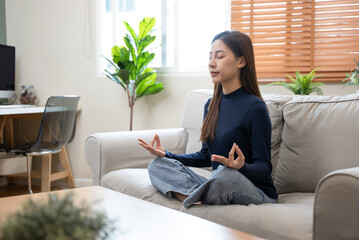well being meditation. Asian women sit in the living room and practice mindfulness by focusing on breath concentrate.