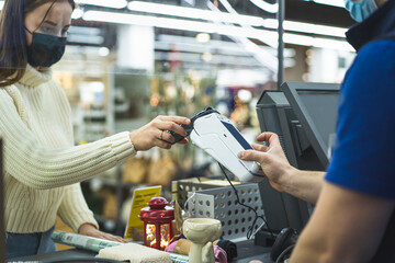 Young woman checks out using the phone through the terminal in the store. Social distancing and coronavirus covid prevention. Maintain a safe distance from others at the store