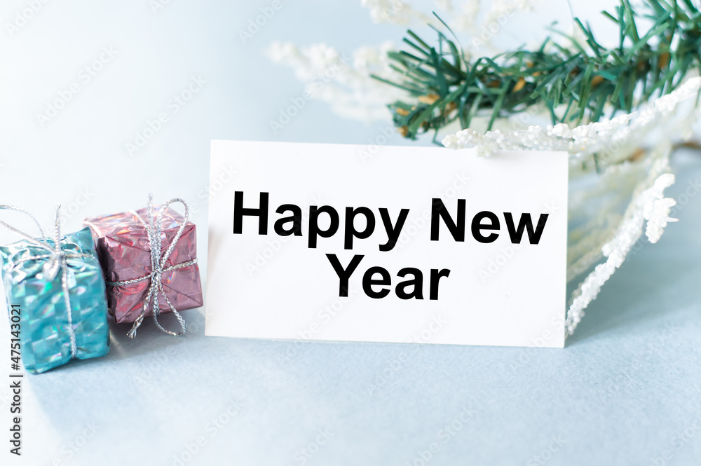 Poster happy new year text on a card on a light background next to two gifts in a package and spruce branch