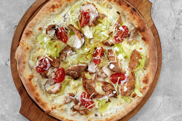 Delicious pizza Caesar style with white sauce, chicken, parmesan, egg, cherry tomatoes and fresh lettuce at wooden background. Restaurant pizzeria menu with delicious taste pizza Caesar.