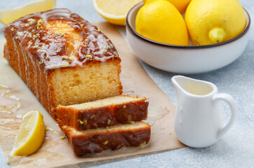 Homemade pound cake loaf with lemon glaze and zest on baking paper on a gray concrete background. Fresh citrus pastries. Selective focus