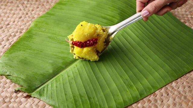 Cooked tapioca or Cassava root Mandioca Aipim  Kappa Indian food woman hand serving on banana leaf 4K video footage. South Indian food served with meat fish curry Asian cuisine  Kerala India Sri Lanka