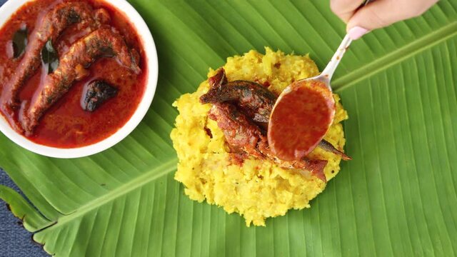tapioca spicy hot Kerala fish curry woman hand serving Indian food banana leaf 4K video footage. Kappa sardine masala fish curry Asian cuisine Bengali macher Jhal Goan fish curry coconut milk cassava 