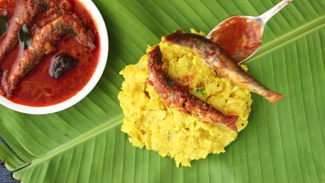 tapioca spicy hot Kerala fish curry woman hand serving Indian food banana leaf 4K video footage. Kappa sardine masala fish curry Asian cuisine Bengali macher Jhal Goan fish curry coconut milk cassava 