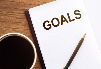 Top view of the text GOALS in notebook, cup of coffee and a pencil on wooden desk