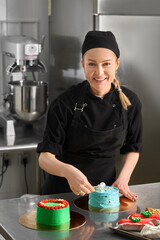 Beautiful and cute girl smiling and decorating cake. Young confectioner wearing black uniform while...