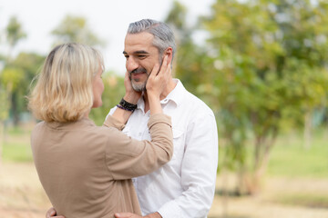 Fototapeta premium Happy couple seniors in love wife touching her husband face and looking at each other while walking in the park.Retirement lifestyle concept