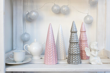 Ceramic figurines of pastel-colored Christmas trees, a white faience angel, a garland of balls made of threads decorate the room before Christmas