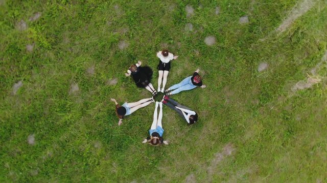 Friends are sitting on the grass with their legs joined in a circle.