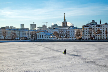 A man walks across the ice of a city pond on a sunny winter day