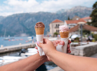 Female and male hand with ice cream in a cone on the background of the old town, Dobrota, Kotor, Montenegro, Europe