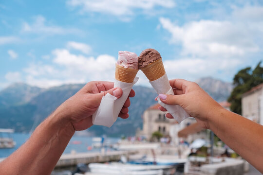 Female and male hand with ice cream in a cone on the background of the old town, Dobrota, Kotor, Montenegro, Europe