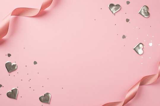 Top view photo of st valentine's day decorations curly silk ribbon silver hearts sequins and heart shaped confetti on isolated pastel pink background with copyspace in the middle
