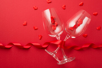 Top view photo of valentine's day decorations red curly ribbon and small hearts flying out of two wineglasses on isolated red background with copyspace