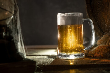 Mug with fresh light beer with foam on wooden vintage background with barrel