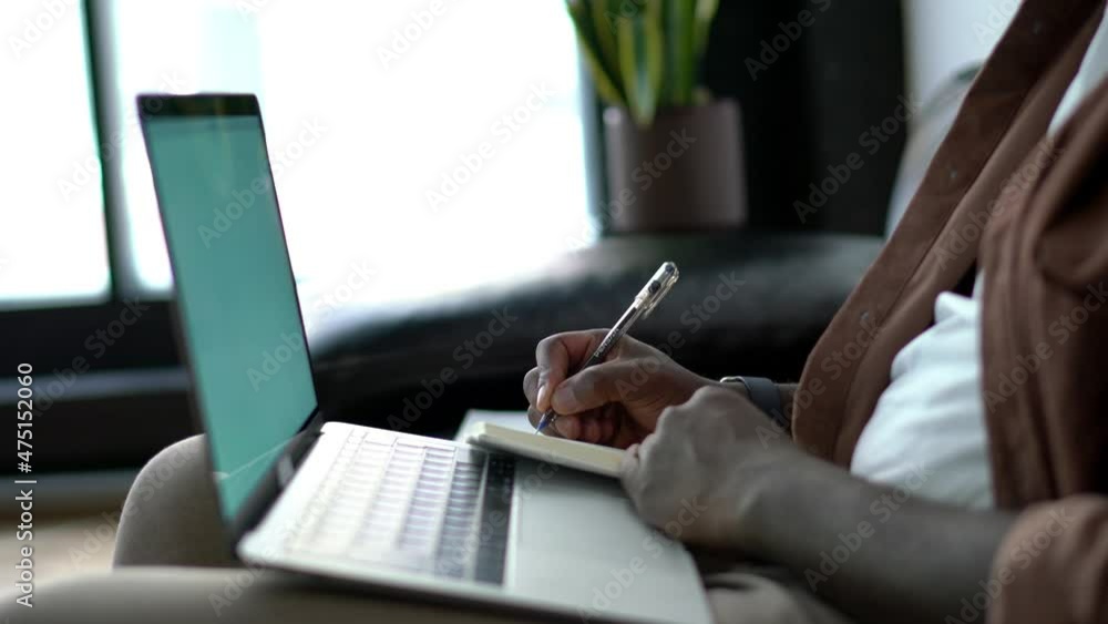 Poster cropped view, african american guy sitting with notepad front open laptop computer while taking note