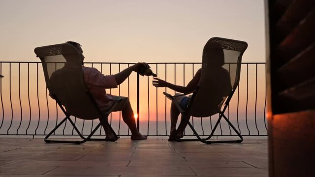 Beautiful young couple drinking wine on the terrace and admiring the sunset over the sea.