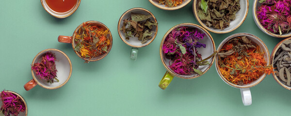 Assortment of dried relaxing tea herbs in colourful cups on mint green background. Calendula, mint,...