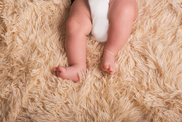 Bare legs of a newborn on a fluffy, light, one-ton, warm covering. Cute newborn baby feet close up
