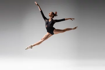  full length of young ballerina in pointe shoes and black bodysuit jumping on dark gray © LIGHTFIELD STUDIOS