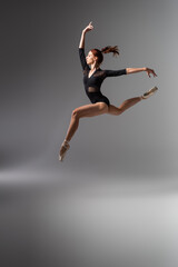 Fototapeta na wymiar pretty ballerina in pointe shoes and black bodysuit jumping on dark grey