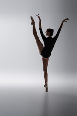 full length of flexible ballerina in bodysuit dancing on dark gray