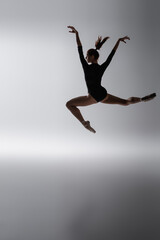 redhead ballerina in bodysuit jumping with outstretched hands on dark gray