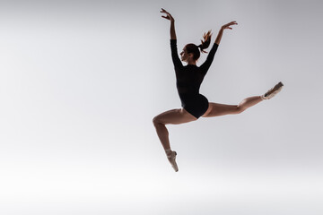 full length of young ballerina in black bodysuit levitating on grey