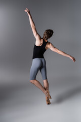 back view of young man in ballet shoes performing ballet dance on dark grey