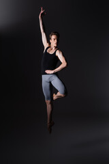 young and graceful dancer gesturing while performing ballet dance while jumping on black